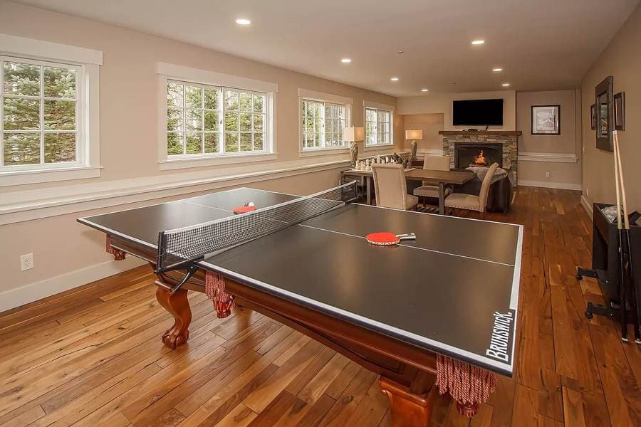 The same room fully finished as a game room with hardwood floors and stone fireplace